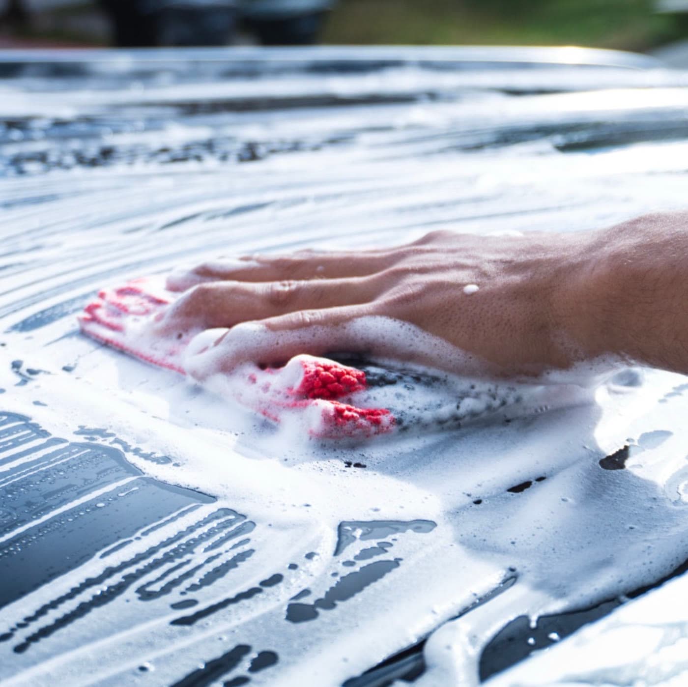 A hand washing dark paint with foam and a wash mitt