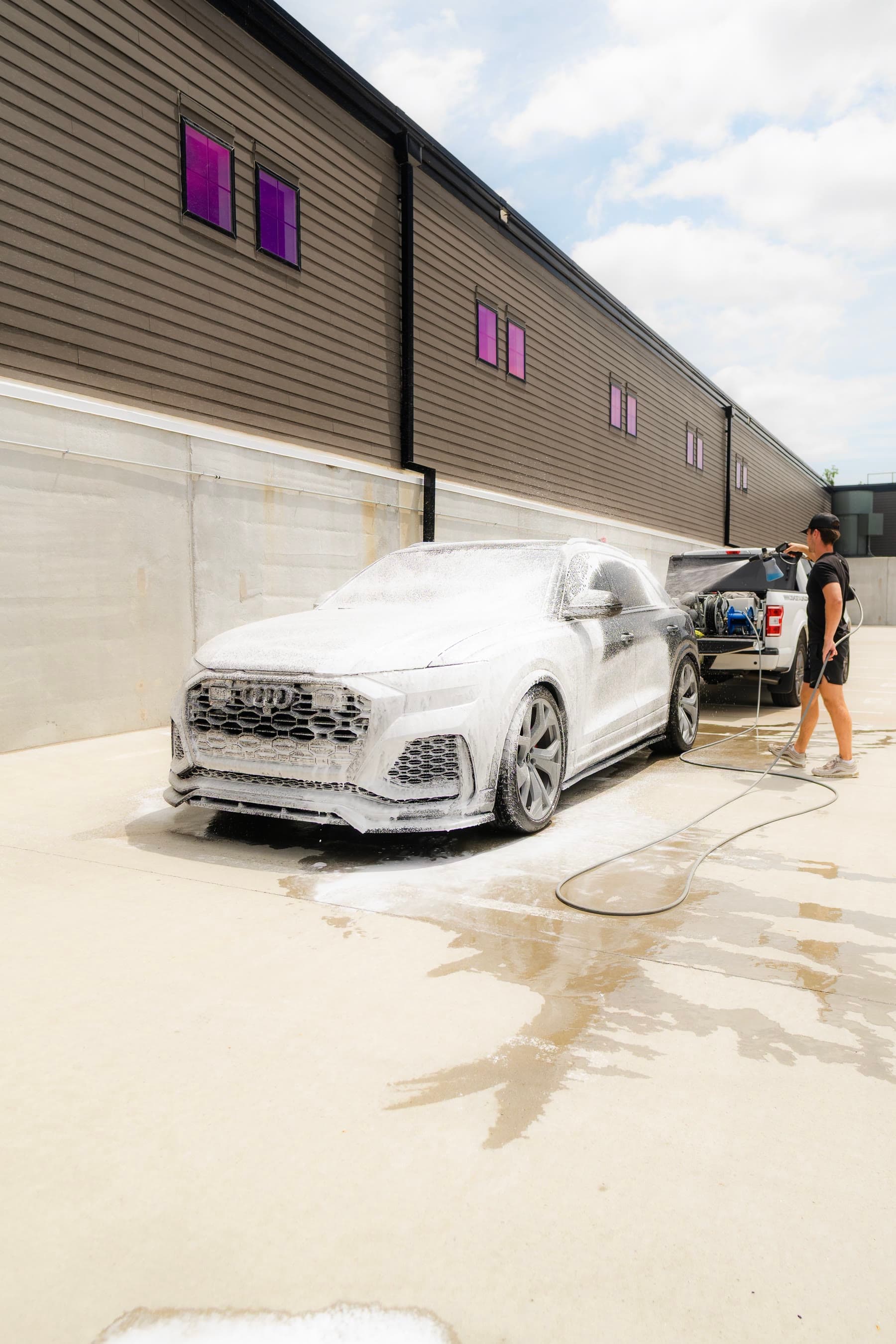 A silver Audi covered in foam while a technician rinses from a truck