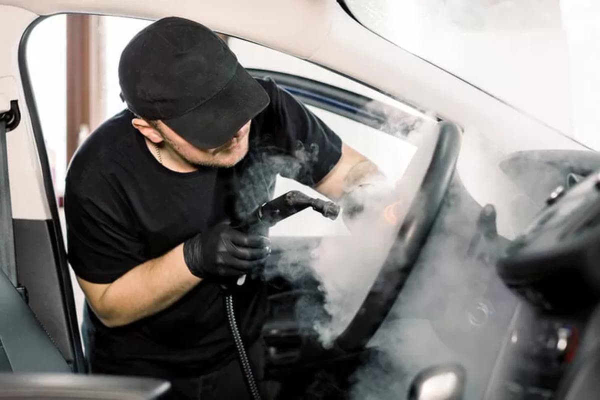 A technician steaming the dashboard and steering wheel of a car