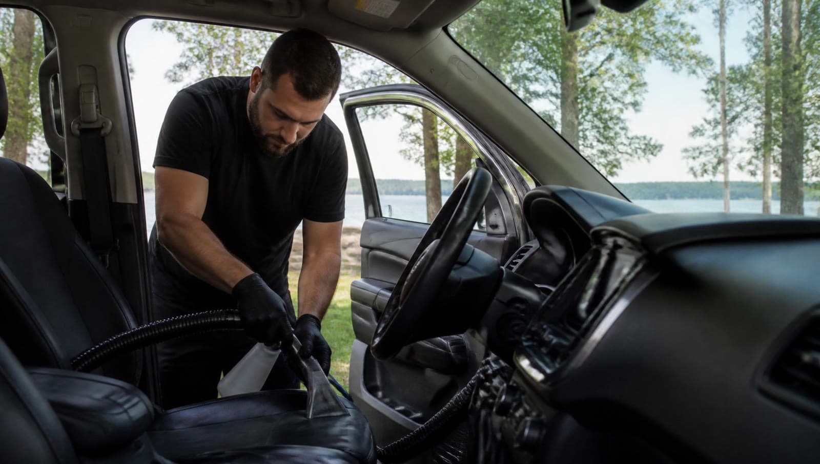 A detailer cleaning an SUV interior, with trees in the background.