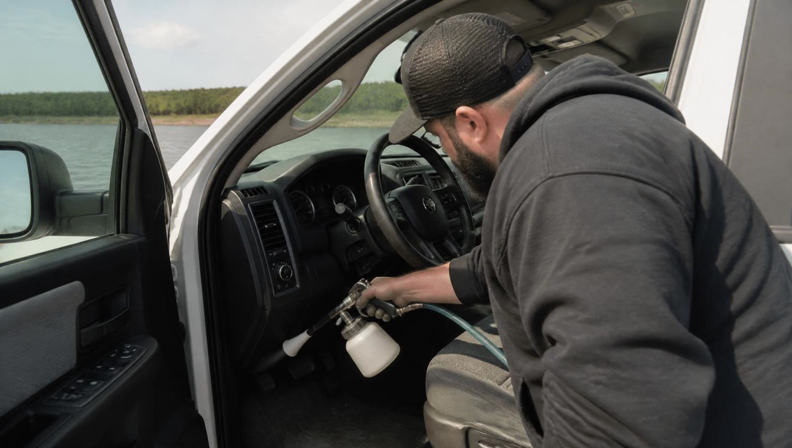 A detailer cleaning a truck interior near trees and water.