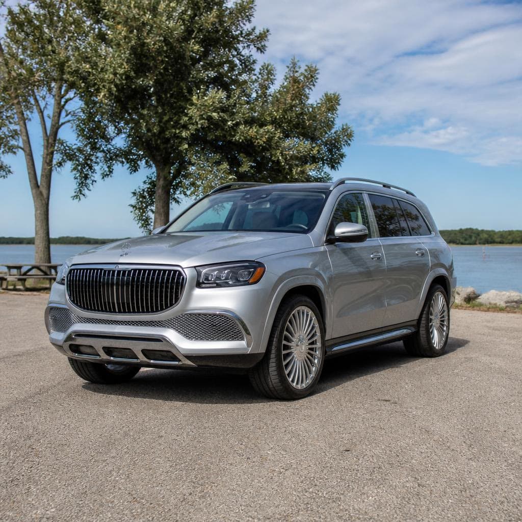 A silver Mercedes SUV with trees and water behind it.